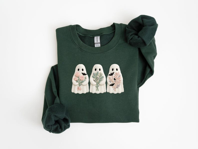 K&ouml;nnte beinhalten: Dunkelgr&uuml;nes Sweatshirt mit drei wei&szlig;en Geistermotiven, die jeweils Blumen- und Fledermausmotive halten. Die Geister haben schwarze Punktaugen. Ein lang&auml;rmliges Oberteil, perfekt f&uuml;r Halloween oder die gruselige Jahreszeit. Bequemes, l&auml;ssiges Kleidungsst&uuml;ck.