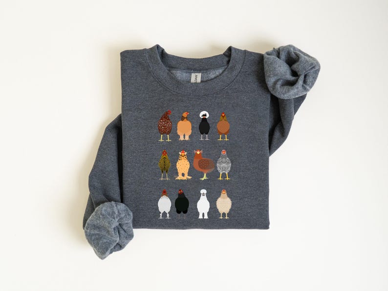 May include: Dark gray sweatshirt featuring a colorful embroidered design of various chicken breeds. The chickens are depicted in a row, each with unique feather patterns and colors. The sweatshirt has long sleeves and a crew neck.