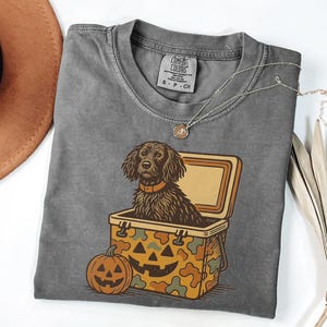 May include: Gray Comfort Colors t-shirt featuring a brown dog inside a jack-o'-lantern cooler. A carved pumpkin sits below the cooler. The shirt has a crew neck and a small tag on the collar.