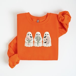 K&ouml;nnte beinhalten: Orangefarbenes Sweatshirt mit Rundhalsausschnitt und drei wei&szlig;en Geisterfiguren. Jeder Geist h&auml;lt einen Blumenstrau&szlig;, einen Zweig Gr&uuml;nzeug und einen Zweig Bl&auml;tter mit Flederm&auml;usen. Das Design hat ein Halloween-Thema.
