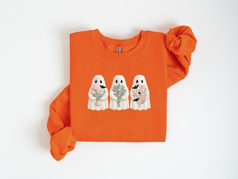 K&ouml;nnte beinhalten: Orangefarbenes Sweatshirt mit Rundhalsausschnitt und drei wei&szlig;en Geisterfiguren. Jeder Geist h&auml;lt einen Blumenstrau&szlig;, einen Zweig Gr&uuml;nzeug und einen Zweig Bl&auml;tter mit Flederm&auml;usen. Das Design hat ein Halloween-Thema.