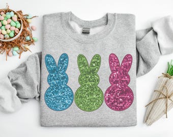 Può includere: Una felpa grigia con tre forme di coniglietto di Pasqua in paillettes. I coniglietti sono blu, verdi e rosa.