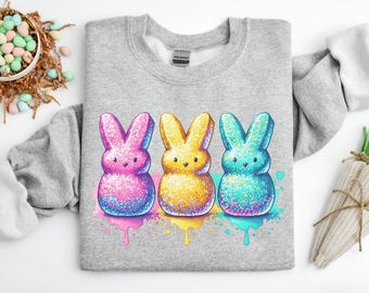 Può includere: Una felpa grigia con una grafica di tre Peeps color pastello a forma di coniglietti. I coniglietti sono rosa, giallo e blu con occhi bianchi e un naso rosa. I coniglietti sono circondati da schizzi di vernice colorati.