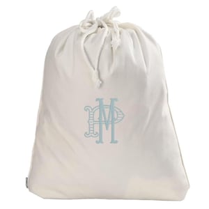 May include: A cream-colored drawstring bag with a light blue monogram. The bag is made of a soft fabric and has a white drawstring closure at the top. The monogram features the letters "P" and "M" in a decorative font.