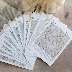 May include: A set of cards with different floral patterns and the word "GRACIOUS" printed on the top card. The cards are arranged in a fan shape on a wooden surface.