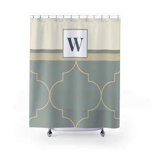 May include: A shower curtain with a geometric pattern in shades of gray and beige. The top section is a solid beige, with a gray stripe below. A white square with the letter "W" in navy blue is centered at the top.
