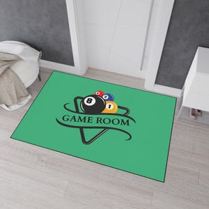 May include: A rectangular green doormat with a black border. The mat features a graphic of billiard balls and the words "GAME ROOM" in black. The billiard balls are numbered 1, 2, and 8, with red, blue, and yellow accents.