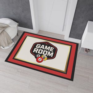 May include: Rectangular doormat with a cream centre featuring a "GAME ROOM" logo and billiard balls. The mat has a red border with gold and black trim. Suitable for a games room or entertainment area. The dimensions are in centimetres.