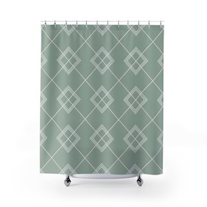 May include: Sage green shower curtain with a geometric diamond pattern in white. The curtain is hanging from a metal rod with silver-colored hooks. The design features intersecting lines and diamond shapes.