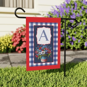 May include: A red, white, and blue garden flag with a floral design and the letter "A". The flag features a gingham border and a vase with an American flag design. The flag is displayed on a black metal stand.
