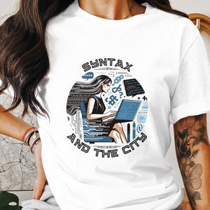May include: White t-shirt featuring a graphic of a woman coding on a laptop. The graphic is enclosed in a circle with the text "SYNTAX AND THE CITY".