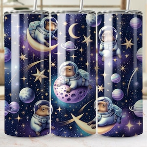 May include: Three stainless steel tumblers with a space-themed design featuring capybaras wearing astronaut suits and floating on planets and moons. The background is a dark blue with stars and a crescent moon.
