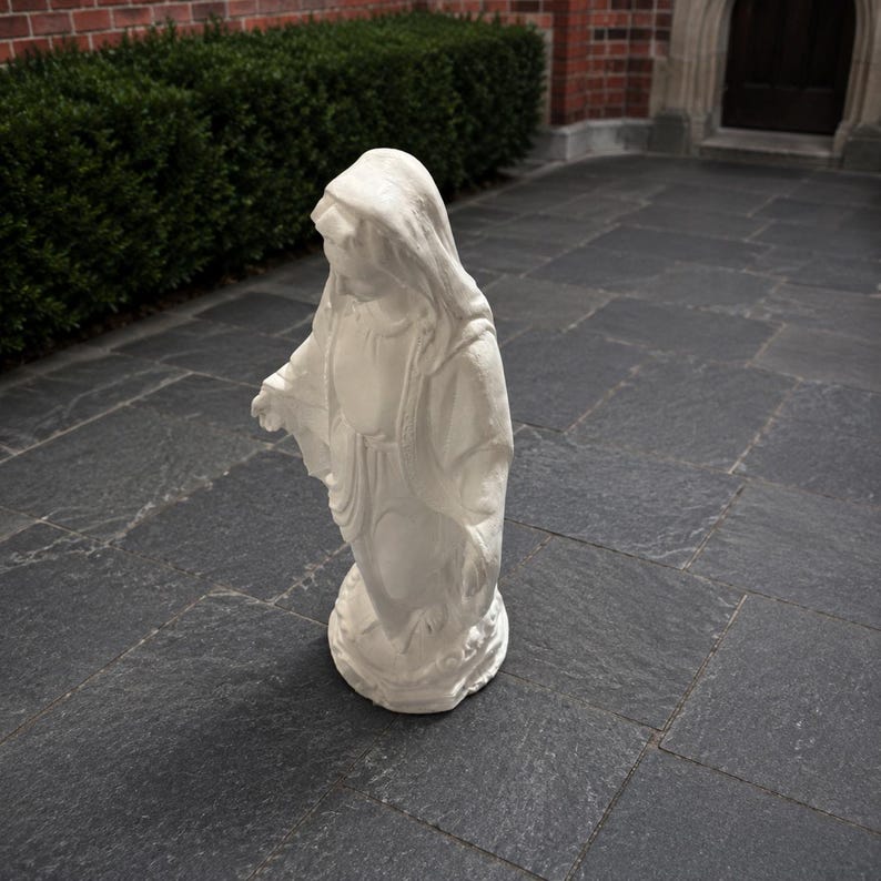May include: A white statue of a figure wearing a hooded robe, standing with arms slightly extended. The sculpture features draped fabric details and rests on a circular base, capturing a serene posture with a smooth, matte finish throughout.