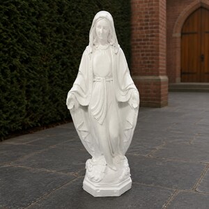 May include: A white statue of the Virgin Mary standing with arms outstretched, wearing a long, flowing robe and a head covering. The figure is positioned on a small, hexagonal base, featuring detailed folds in the fabric and a serene facial expression.