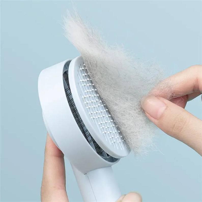 May include: A white pet grooming brush with a handle, designed to remove loose fur. The brush head features closely spaced, fine bristles. A large clump of collected fur is being removed from the brush, showing the effectiveness of the tool.