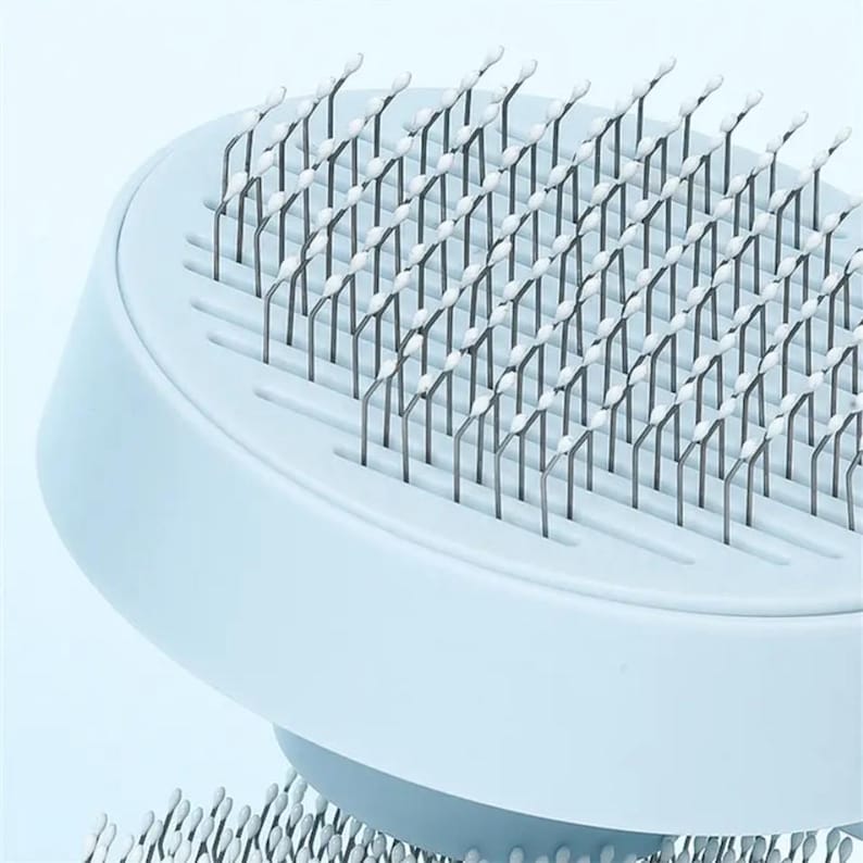May include: A light blue pet grooming brush with numerous thin, metal bristles topped with white tips. The brush has a rounded shape with a handle and is designed for removing loose fur and tangles from pets.