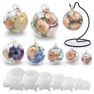 May include: Clear glass baubles filled with dried flowers in shades of pink, yellow, and purple. Some baubles are displayed on white stands, and one is suspended from a black metal stand. Various sizes are shown.