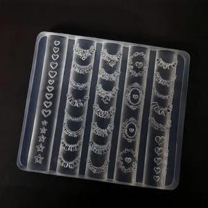 Peut inclure: Un moule en silicone transparent avec divers motifs de colliers et de breloques. Le moule présente des formes de cœur, d'étoile et de collier décoratif. Les motifs sont disposés en colonnes, de forme rectangulaire, sur fond sombre.