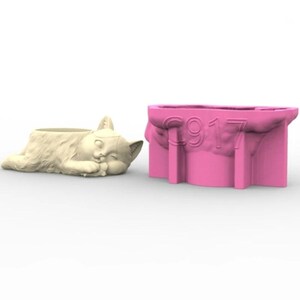 Può includere: Uno stampo in silicone rosa per realizzare un vaso a forma di gatto che dorme. Lo stampo ha il numero "C917" in rilievo. Il vaso finito è mostrato in color crema.