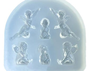 May include: A clear, flexible silicone mold featuring six cherub designs. The cherubs are in various poses, including seated, kneeling, and flying, with detailed wings and facial features. The mold has a light blue hue.