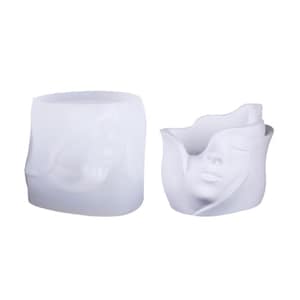 Pode incluir: Duas floreiras brancas em forma de rosto. Uma tem formato cilíndrico com um rosto esculpido na lateral. A outra é uma floreira em forma de tulipa com um rosto esculpido na frente. Ambas são feitas de material liso e fosco.