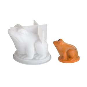 May include: A white frog-shaped mold with a cross-shaped insert and a small orange frog figurine. The mold is made of a smooth, opaque material, while the figurine is a solid, glossy orange. The frog figurines are likely for crafts or decoration.