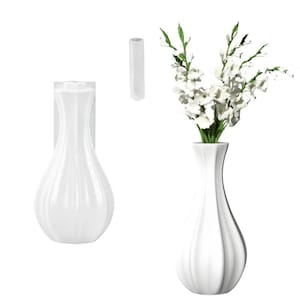 Könnte beinhalten: Weiße Keramikvase mit bauchigem Boden und schlankem Hals, die weiße Blumen mit grünen Stielen enthält. Eine ähnliche Vase ist auf einer weißen Rückwand montiert, und ein zylindrisches Stück ist ebenfalls abgebildet. Die Vasen haben ein geripptes Design.