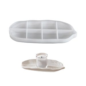 May include: Two white decorative trays are shown. One is a large, divided tray. The other is a small, leaf-shaped tray holding a clear glass candle holder with a lit candle. The items are on a white background.