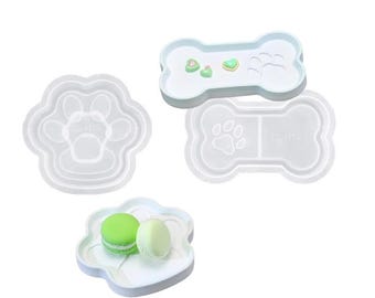 Può includere: Tre stampi in silicone bianco per realizzare artigianato in resina. Uno stampo è a forma di impronta di zampa, un altro è a forma di osso e il terzo è a forma di impronta di zampa con un'impronta di zampa più piccola all'interno.