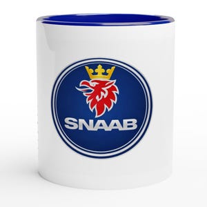 May include: White ceramic coffee mug with a blue interior. The mug features a circular emblem with a red griffin wearing a gold crown, and the word "SNAAB" in white text on a blue background.