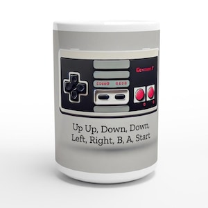 May include: A white ceramic mug featuring a classic video game controller design. The controller is black, gray, and red, with the text "Up Up, Down, Down, Left, Right, B, A, Start" printed below. A nostalgic gift.