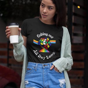 May include: A woman wearing a black t-shirt with a rainbow Rubik's cube graphic and the text "Cubing out All Day Long".