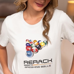 May include: White t-shirt with a graphic of a pool ball rack and the text "RERACK BREAKING BALLS".