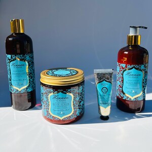 May include: A set of four bath and body products in a Moroccan-inspired design. The products include a shower gel, body scrub, body milk, and hand cream. The bottles and jars are all brown with gold accents and feature a blue and white pattern. The products are labeled "Hammam El Hana" and "PIELOR".