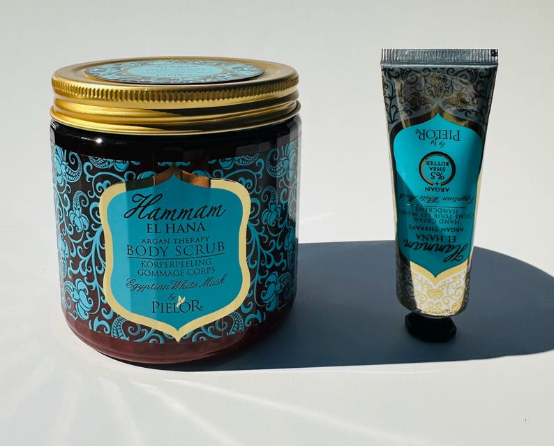 May include: A set of two bath products in a blue and gold design. The larger jar is a body scrub with the text "Hammam El Hana Argan Therapy Body Scrub Korperpeeling Gommage Corps Egyptian White Mask Pielor". The smaller tube is a hand cream with the text "Hammam El Hana Argan Therapy Hand & Nail Cream Moisturizing Pielor".