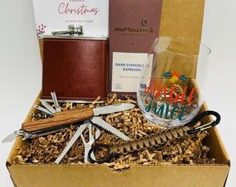 May include: A brown cardboard box filled with a Christmas gift set. The set includes a brown leather flask, a multi-tool knife, a glass with "Jingle Juice" written on it, a bar of dark chocolate espresso, and a card that says "Merry Christmas & Happy New Year".