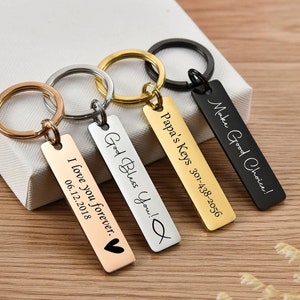 May include: Four gold, silver, and black keychains with engraved messages. The messages include "Make Good Choice!", "Papa's Keys 301-438-2056", "God Bless You!" and "I love you forever. 06.12.2018".