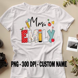 May include: White t-shirt with the name "Emily" in colorful, playful letters. The design includes pencils, hearts, and apples, with the text "Mrs." above the name. The shirt also has the text "PNG - 300 DPI - CUSTOM NAME" at the bottom.
