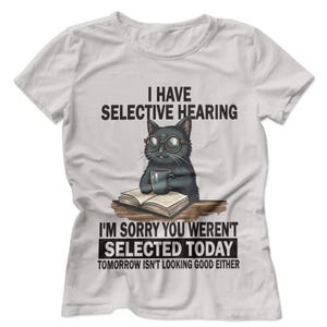 以下が含まれることがあります： 「I HAVE SELECTIVE HEARING」の文字と、メガネをかけた黒猫がマグカップを持っているイラストがプリントされた白いTシャツ。「I'M SORRY YOU WEREN'T SELECTED TODAY TOMORROW ISN'T LOOKING GOOD EITHER」の文字も含まれています。