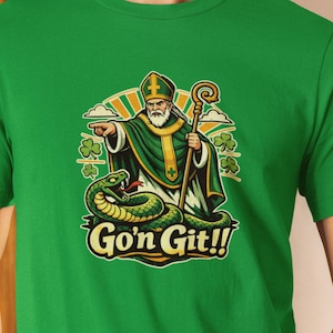 May include: Green t-shirt featuring a cartoon illustration of a saint with a staff, pointing at a green snake. The saint wears a green robe and hat. The text "Go'n Git!!" is below the illustration, with shamrocks.