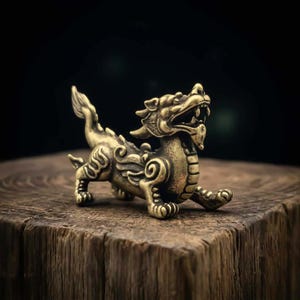 May include: A detailed brass figurine of a mythical creature, possibly a dragon or a similar beast. The sculpture is golden-toned, with intricate details on its body, including scales and swirling patterns. It is posed on a wooden surface against a dark background.