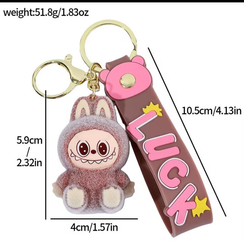 May include: A novelty keychain featuring a cartoon character in a bunny suit. The keychain has a brown strap with the word "LUCK" in pink. The character is 2.32 inches tall and 1.57 inches wide. The strap is 4.13 inches long.