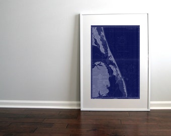 May include: A framed vintage nautical chart of the Outer Banks, North Carolina coastline. The chart is printed in blue and white on a dark blue background. The chart is framed in a white frame.