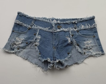 May include: Light blue denim shorts with distressed detailing. The shorts feature a frayed hem, multiple rips, and metal stud accents. The design includes front and back pockets and a button closure.