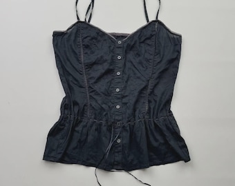 May include: A dark navy blue camisole top with thin spaghetti straps. The top features a button-down front, a cinched waist with a drawstring, and a ruffled hem. The fabric appears to have a subtle textured pattern.