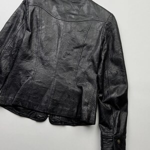 以下が含まれることがあります： ボタン留めのフロントと長袖の黒い革のジャケット。ジャケットは少し短く、テクスチャのある革のデザインが特徴です。