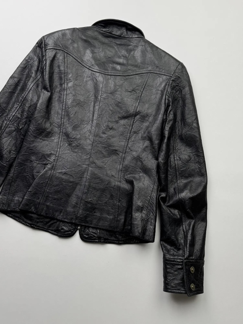 以下が含まれることがあります： ボタン留めのフロントと長袖の黒い革のジャケット。ジャケットは少し短く、テクスチャのある革のデザインが特徴です。