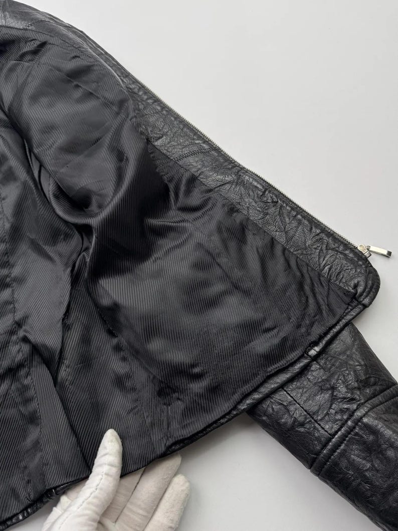 以下が含まれることがあります： 黒い革のジャケットで、ジッパーで閉めることができます。黒い裏地が付いています。ジャケットは裏返して裏地を見ることができます。
