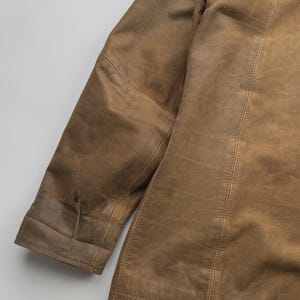 Pu&ograve; includere: Una giacca in pelle color cuoio con maniche lunghe, polsini cuciti e dettagli con cuciture verticali lungo il pannello frontale. Il capo presenta una consistenza liscia e opaca con variazioni naturali sulla superficie in pelle marrone chiaro.