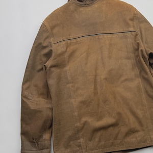 Pu&ograve; includere: Una giacca in camoscio color marrone chiaro con colletto alto, maniche lunghe e una cucitura orizzontale sulla parte superiore della schiena. Il capo presenta dettagli di cuciture visibili lungo i pannelli verticali e una texture liscia e opaca.
